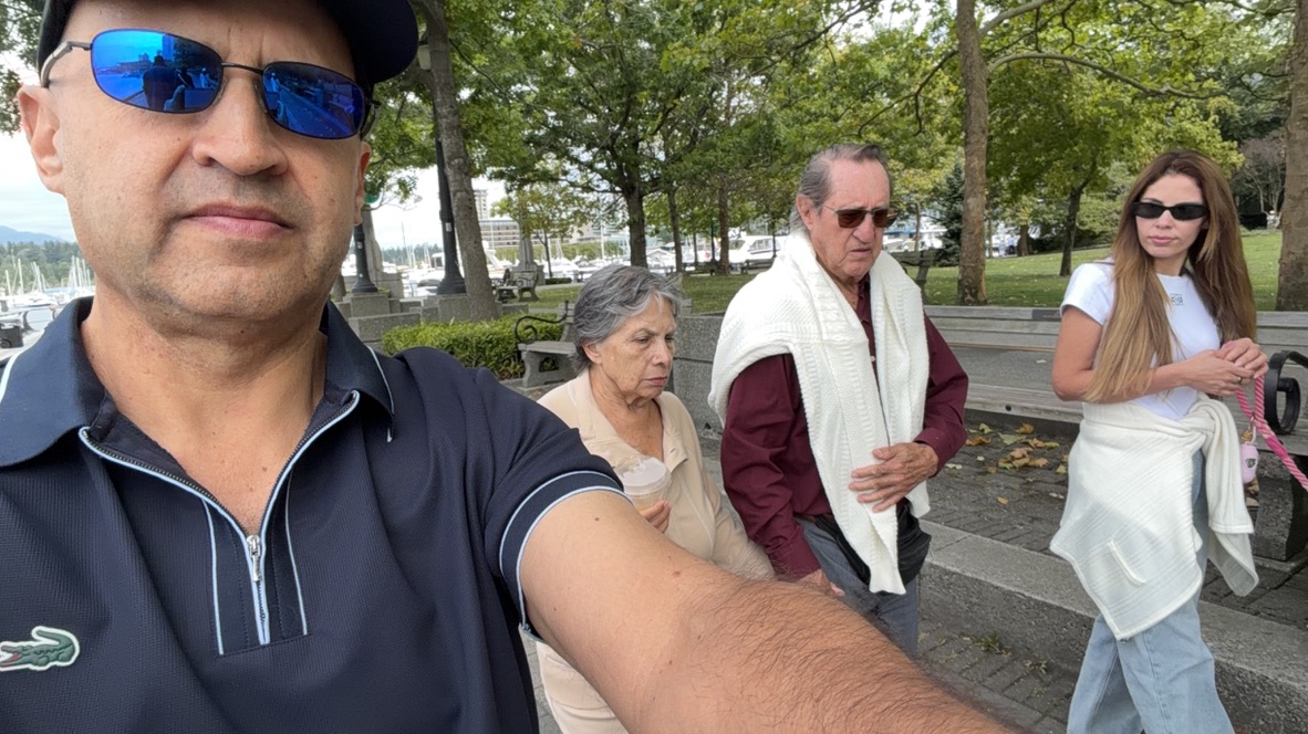 Fabian de la Fuente taking a group selfie in a scenic park in Vancouver, BC, with a marina and sailboats in the background.